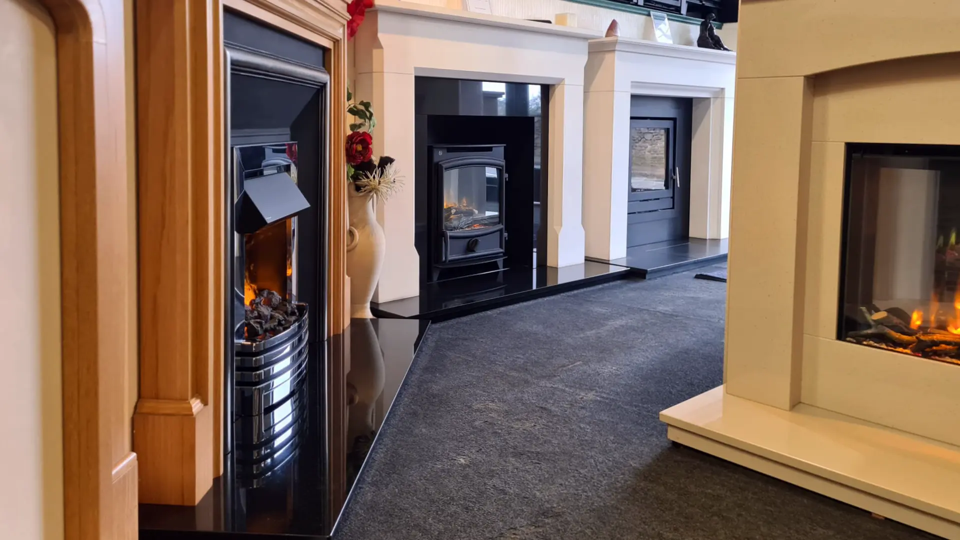 A row of fireplace displays in the Warm Interiors showroom, each with a lit gas fire set into a surround